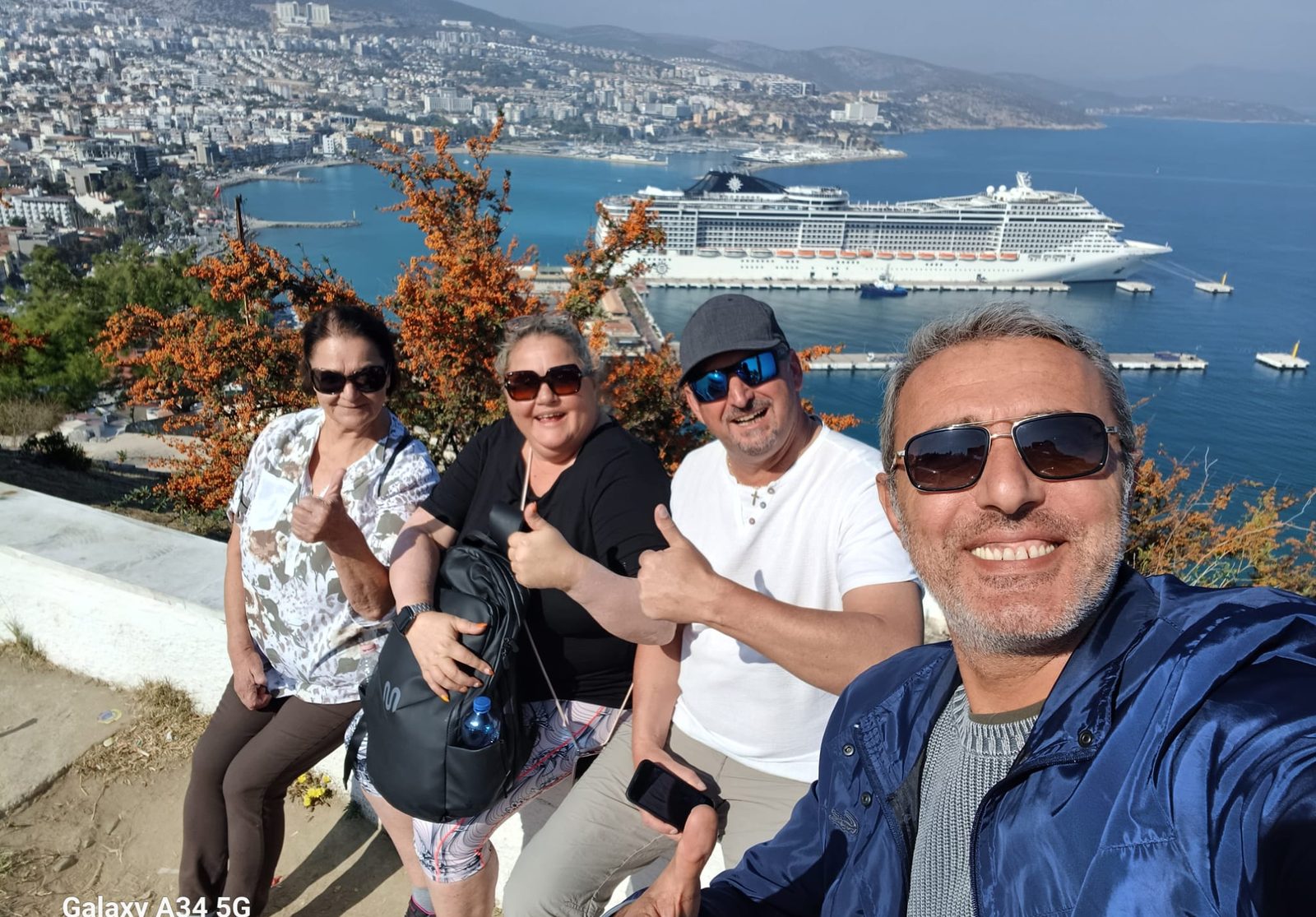 Akın mit zufriedenen Gästen über dem Kreuzfahrthafen Kuşadası, ihr Schiff in der Bucht